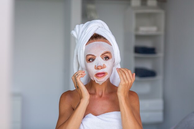 Retrato de mujer bonita caucásica tranquila con una toalla en la cabeza y una máscara cosmética en la cara Concepto de cuidado de la piel de la cara Mujer relajarse en la cama en casa
