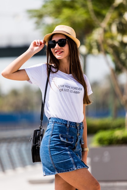 Retrato de mujer bonita con gafas de sol y sombrero de paja posando en el verano de la ciudad