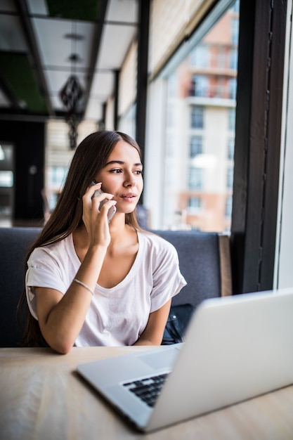 Foto gratuita retrato de mujer bonita hablando por teléfono mientras está sentado en la cafetería y disfrutando de un café