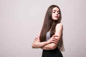 Foto gratuita retrato de mujer bonita joven con estilo sonriendo en camiseta gris en la pared blanca, aspecto aislado, natural, cabello largo y castaño, brazos cruzados