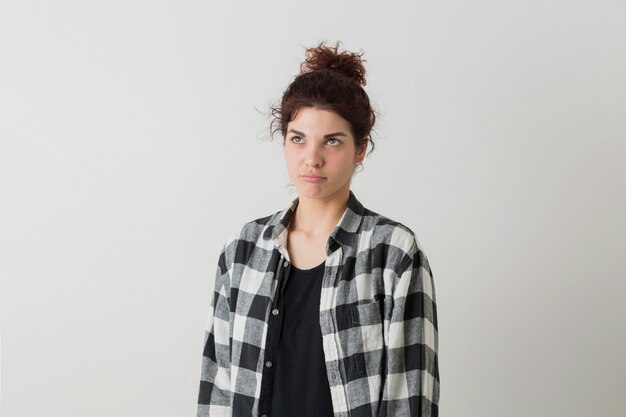 Retrato de mujer bonita joven inconformista en camisa a cuadros pensando, teniendo un problema, posando aislado sobre fondo blanco de estudio