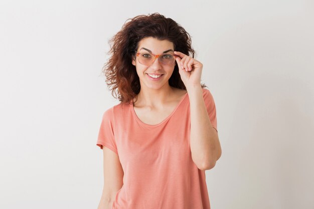 Retrato de mujer bonita joven inconformista natural con peinado rizado en camisa rosa posando con gafas aisladas sobre fondo blanco de estudio, expresión de la cara emocionada