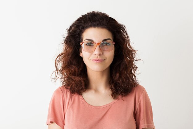 Retrato de mujer bonita joven inconformista natural con peinado rizado en camisa rosa posando con gafas aisladas sobre fondo blanco de estudio