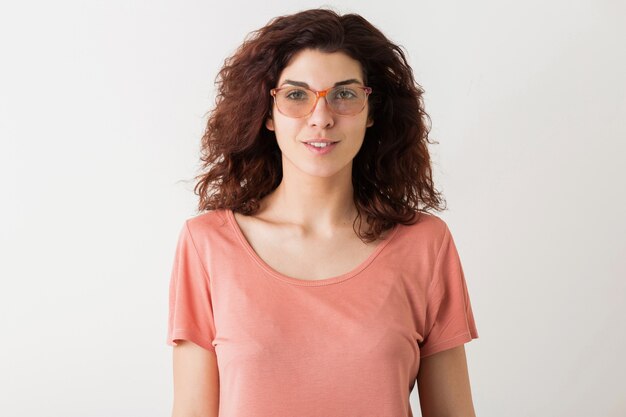 Retrato de mujer bonita joven inconformista natural con peinado rizado en camisa rosa posando con gafas aisladas sobre fondo blanco de estudio