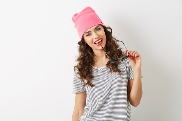 Retrato de mujer bonita joven inconformista con sombrero rosa, sosteniendo gafas de sol, sonriente, feliz, aislado, sexy, coqueta, pelo curlu de cerca