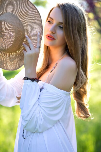 Retrato de mujer bonita joven sensible con cabello largo, en un atractivo vestido blanco claro con sombrero de verano, disfrutando de la luz del sol con los ojos cerrados. Expresando verdaderas emociones positivas, inspiraciones.