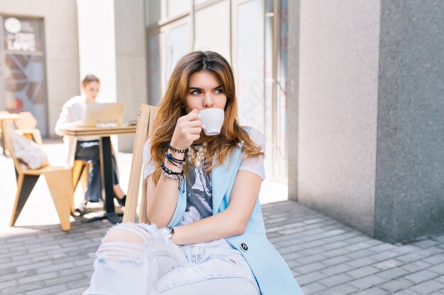 Retrato de mujer bonita con pelo largo sentado en una silla en el café al aire libre