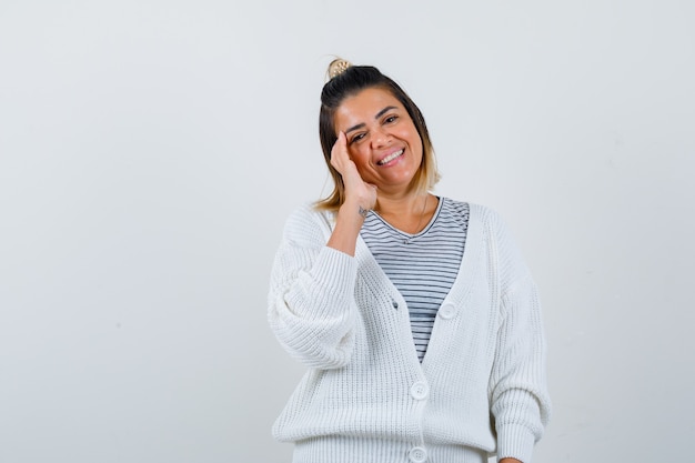 Retrato de mujer bonita posando con la mano al lado de la cara en camiseta, chaqueta de punto y mirando jovial