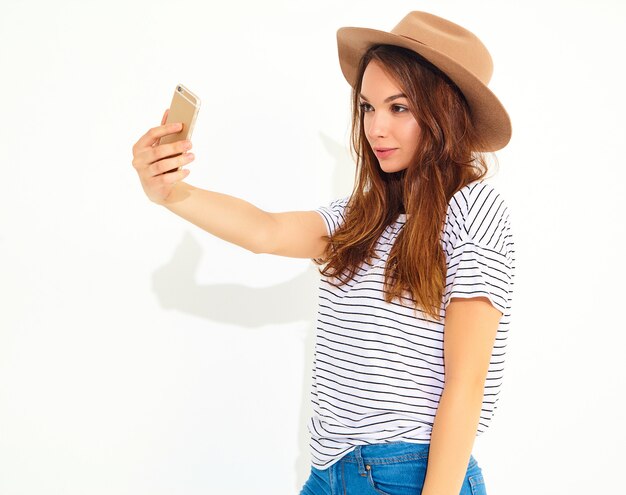 Retrato de una mujer bonita en ropa hipster de verano tomando un selfie aislado en la pared blanca