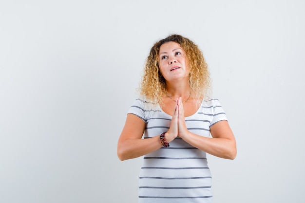 Retrato de mujer bonita rubia mostrando gesto de namaste en camiseta a rayas y mirando pensativo vista frontal