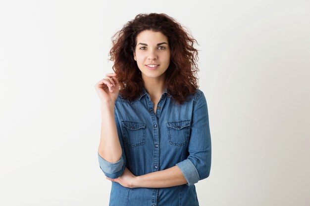 Retrato de mujer bonita sonriente joven inconformista natural con peinado rizado en camisa de mezclilla posando aislado sobre fondo blanco de estudio