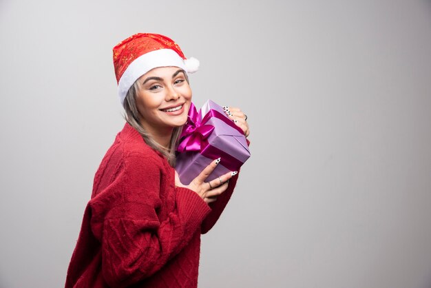 Retrato de mujer con caja de regalo sonriendo sobre fondo gris.