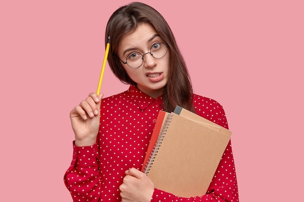 Retrato de mujer con camisa roja y anteojos redondos sosteniendo blocs de notas