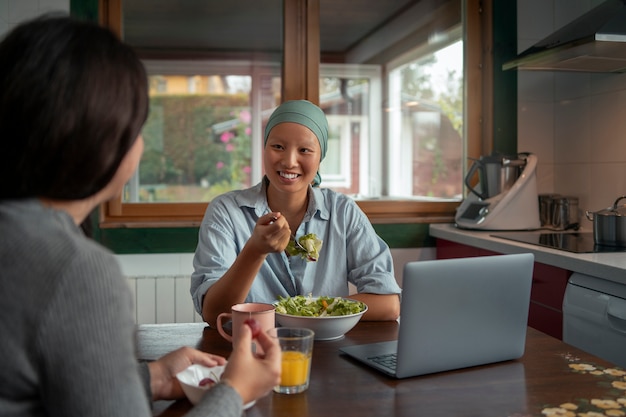 Foto gratuita retrato de una mujer con cáncer usando una computadora portátil con un amigo en casa