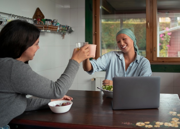 Retrato de una mujer con cáncer usando una computadora portátil con un amigo en casa