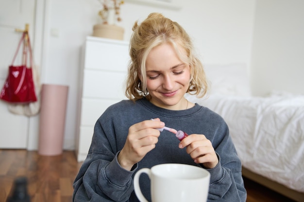 Foto gratuita retrato de una mujer carismática sonriente que se pone brillo para los labios, bebe té y graba video en una cámara digital.