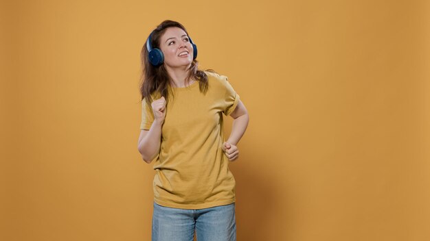 Retrato de mujer casual escuchando música alegre en auriculares inalámbricos y haciendo movimientos de baile extravagantes en el estudio. Mujer positiva llena de energía con auriculares haciendo fiesta y bailando sola.