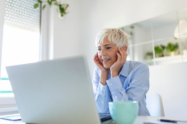 Retrato de una mujer casual que usa su computadora portátil mientras está sentada en la oficina en casa y trabajando Una atractiva mujer de negocios de mediana edad sentada frente a la computadora portátil y administrando su pequeña empresa desde casa