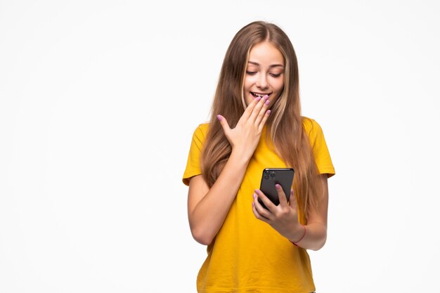 Retrato de una mujer casual sonriente sosteniendo smartphone sobre pared blanca