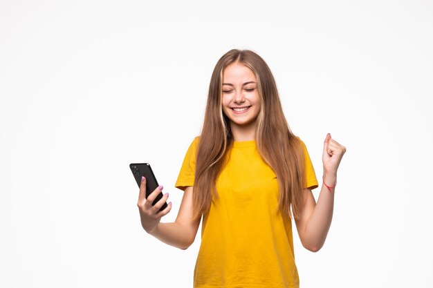 Retrato de una mujer casual sonriente sosteniendo smartphone sobre pared blanca