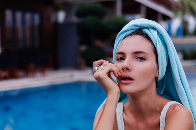 Retrato de mujer caucásica joven delgada en forma en bikini azul fuera de villa junto a la piscina en día lluvioso