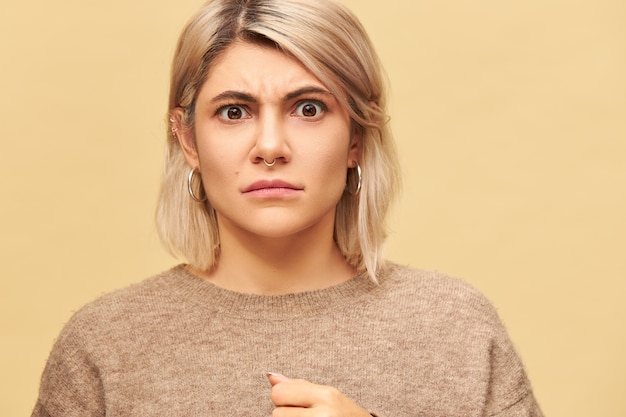 Retrato de mujer caucásica joven enojada enojada con estilo que lleva piercing facial y cejas fruncidas del suéter caliente que está de mal humor, demostrando su desaprobación y descontento. Emociones negativas