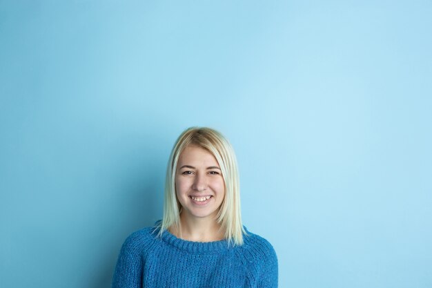 El retrato de la mujer caucásica joven parece soñadora, linda y feliz. Pensando, preguntándose, soñando sobre fondo azul de estudio. Copyspace para su anuncio. Concepto de futuro, destino, sueños, visualización.