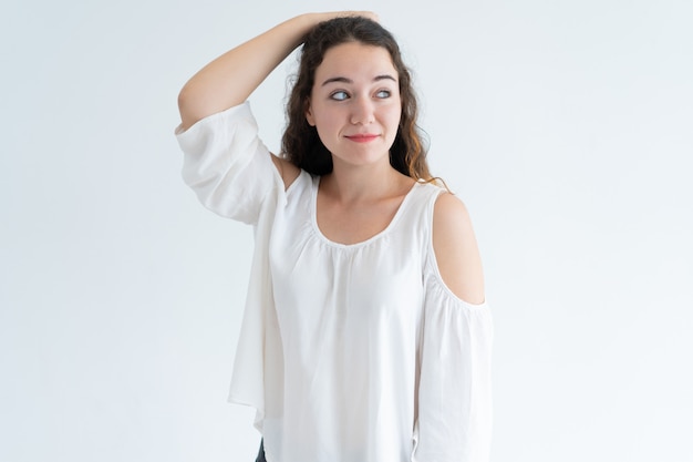 Retrato de la mujer caucásica joven sonriente que rasguña la cabeza