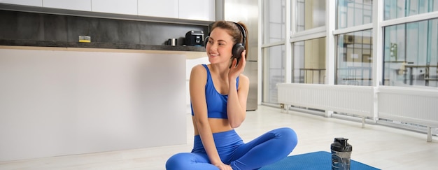 Foto gratuita retrato de mujer en chándal haciendo ejercicios de yoga en casa con auriculares inalámbricos