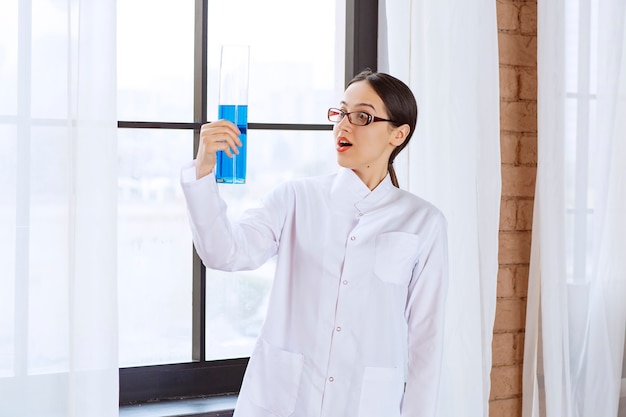 Foto gratuita retrato de mujer científica en bata de laboratorio con líquido químico azul.