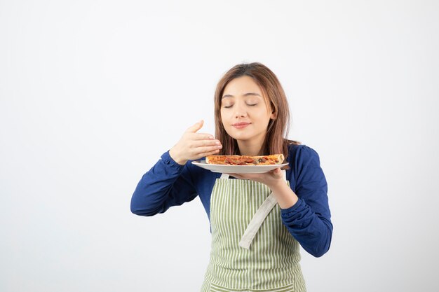 Retrato de mujer cocinera en delantal huele rebanadas de pizza en blanco