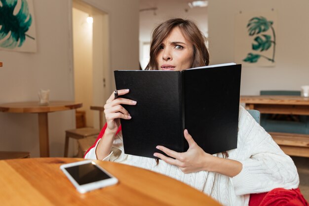 Retrato de una mujer confundida con bloc de notas de portada en blanco