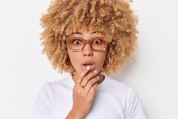 Retrato de mujer conmocionada mantiene la boca abierta de asombro no puedo creer en noticias sorprendentes retiene la respiración a través de gafas vestidas casualmente aisladas sobre fondo blanco. Reacciones humanas