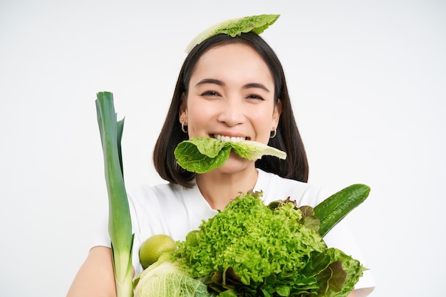 Retrato de una mujer coreana sonriente come hojas de lechuga sosteniendo vegetales verdes comiendo alimentos nutritivos w