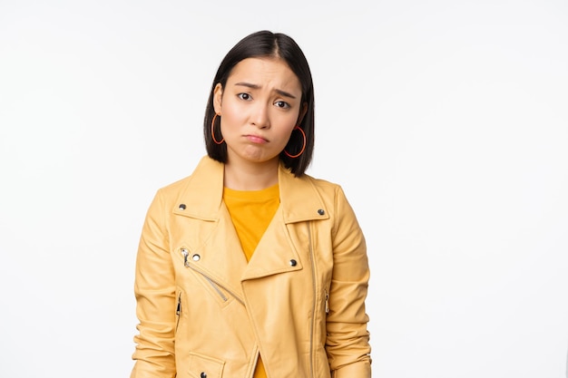 Retrato de una mujer coreana triste que se enfurruña con el ceño fruncido y se ve disgustada angustiada expresión de la cara frustrada de pie sombría contra el fondo blanco