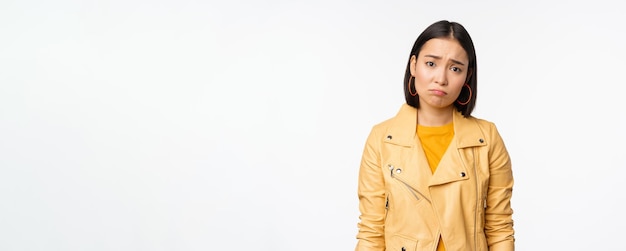 Retrato de una mujer coreana triste que se enfurruña con el ceño fruncido y se ve disgustada angustiada expresión de la cara frustrada de pie sombría contra el fondo blanco