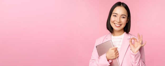 Retrato de mujer corporativa chica en oficina en traje de negocios sosteniendo tableta digital mostrando bien reco