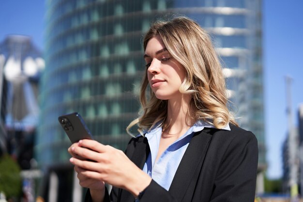 Retrato de una mujer corporativa confiada que usa un teléfono móvil en la calle de la ciudad empresaria que envía mensajes en s