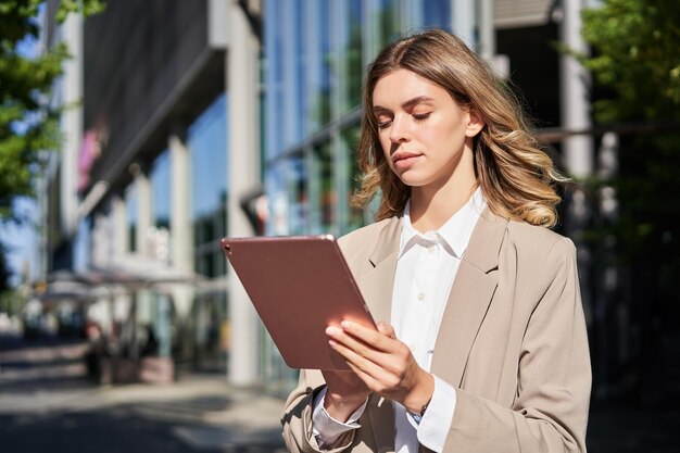 Retrato de mujer corporativa lee trabajos de noticias en su tableta digital mientras se dirigía a la oficina stansd