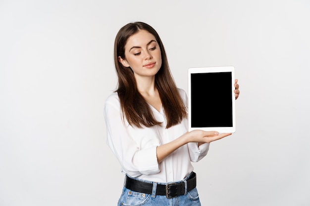 Retrato de mujer corporativa mostrando la pantalla de la tableta, demostrando el sitio web de la empresa, de pie sobre fondo blanco.