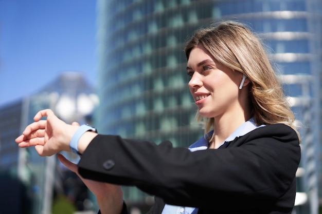 Foto gratuita retrato de una mujer corporativa ocupada con auriculares inalámbricos mirando la hora en su registro de reloj digital