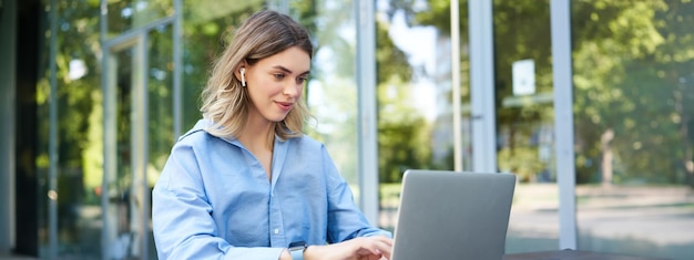 Foto gratuita retrato de una mujer corporativa que trabaja fuera de la oficina sentada a distancia con auriculares inalámbricos para portátiles