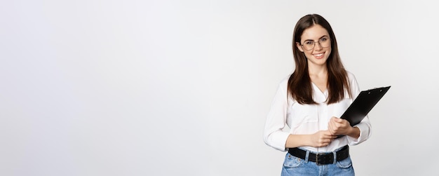 Foto gratuita retrato de mujer corporativa sosteniendo portapapeles en el trabajo de pie en traje formal sobre fondo blanco