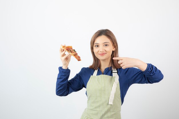 Retrato de mujer en delantal apuntando a la rebanada de pizza en blanco
