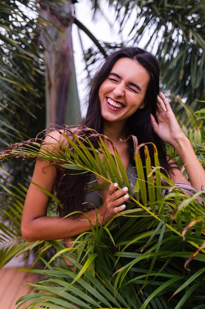 Retrato de mujer delgada bronceada en forma en bikini pequeño verde posando con hojas tropicales