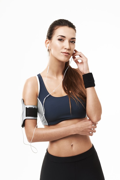 Retrato de mujer deportiva en auriculares y ropa deportiva posando en blanco.