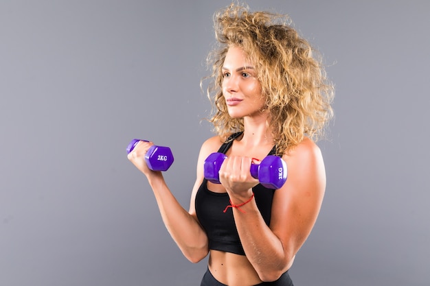 Foto gratuita retrato de mujer deportiva delgada haciendo ejercicios con pequeñas pesas aisladas sobre pared gris