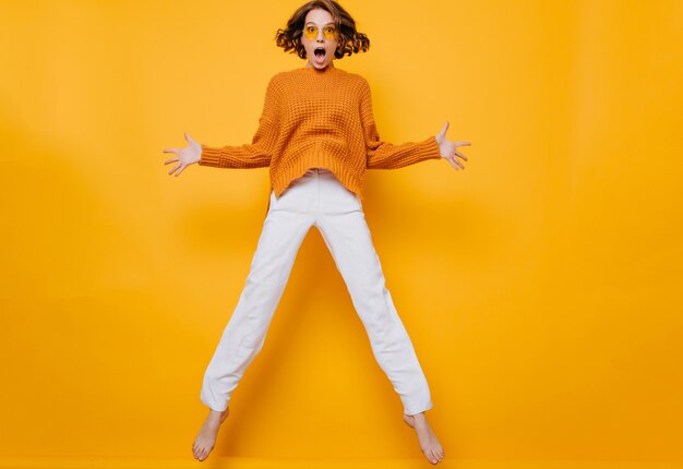 Retrato de mujer divertida en pantalones blancos jugando sobre fondo amarillo