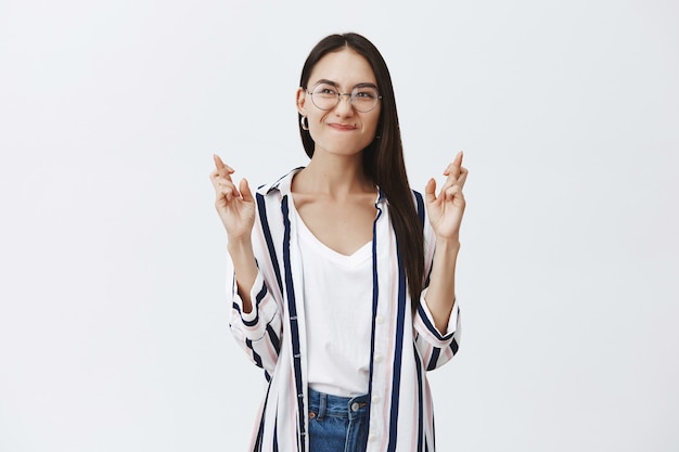 Foto gratuita retrato de mujer elegante y guapa en gafas y blusa de moda, frunciendo los labios y frunciendo el ceño mientras espera o pide un deseo