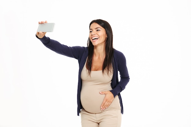 Retrato de una mujer embarazada alegre tomando selfie